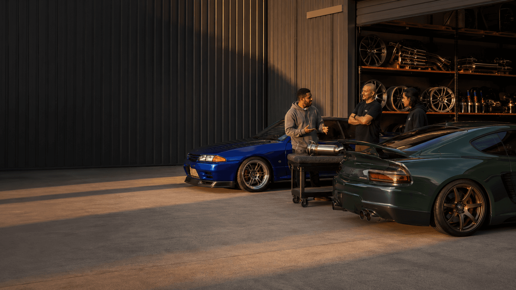 Owners talking beside performance cars and a parts trolley at the KICKBACK warehouse